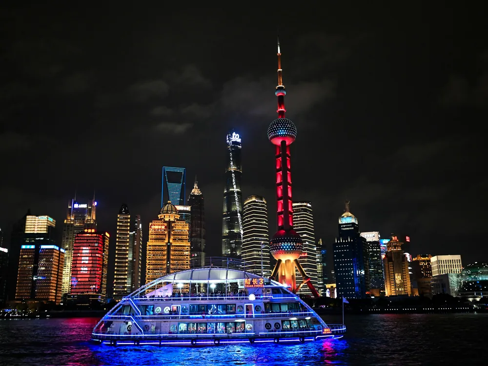 A cruise boat outlined in blue light on the Huangpu at night, with the red Oriental Pearl Tower and Pudong's towers behind it