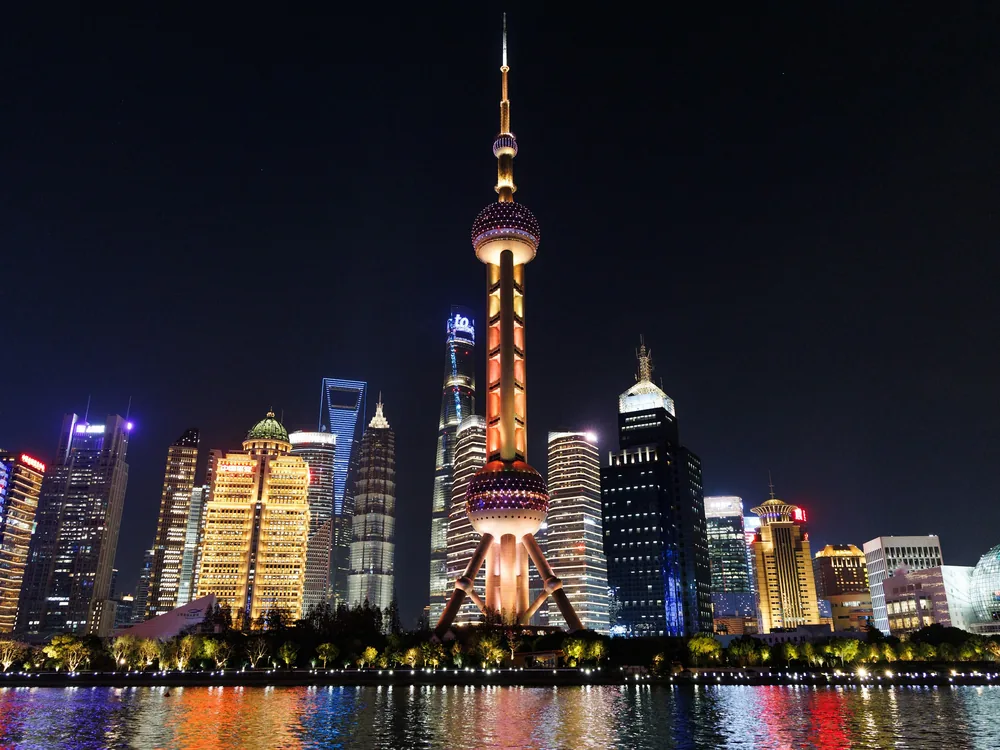 The Oriental Pearl Tower lit gold and orange above the Pudong waterfront, seen from the river, with other towers around it